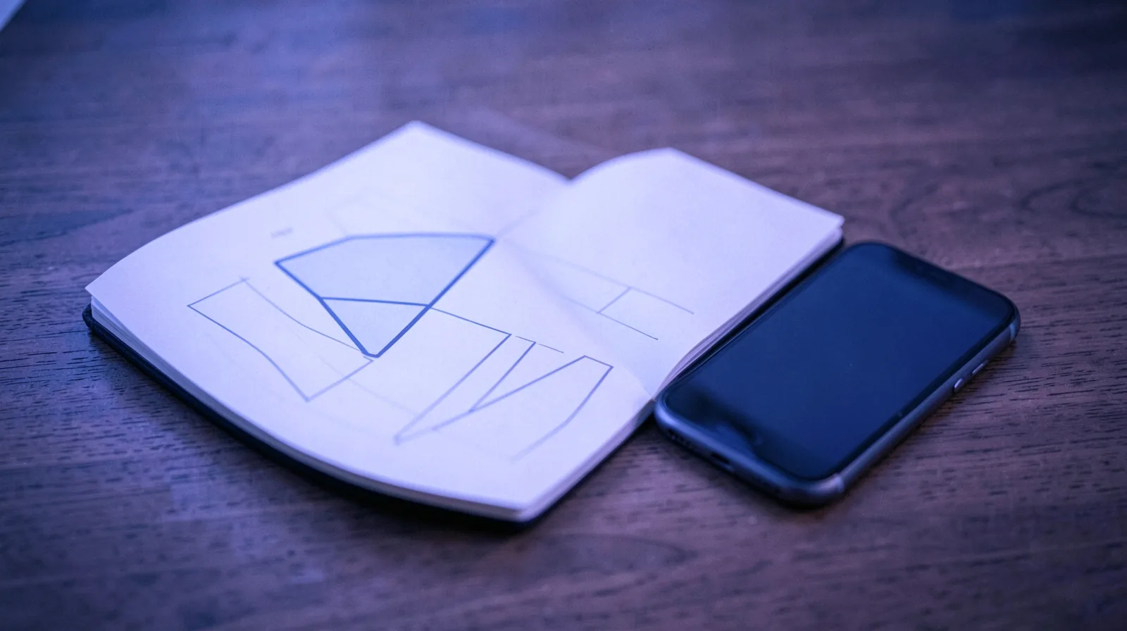 Caderno aberto com esboço de um funil de vendas abstrato e celular ao lado sobre a mesa