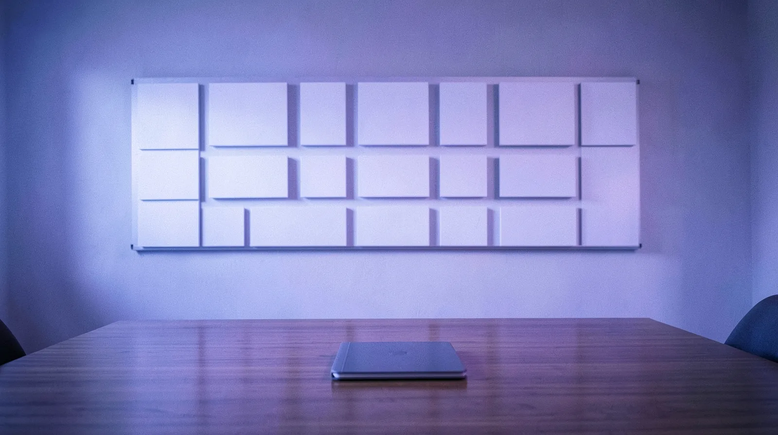 Quadro com colunas de cartões em branco diante de uma mesa de reunião com notebook