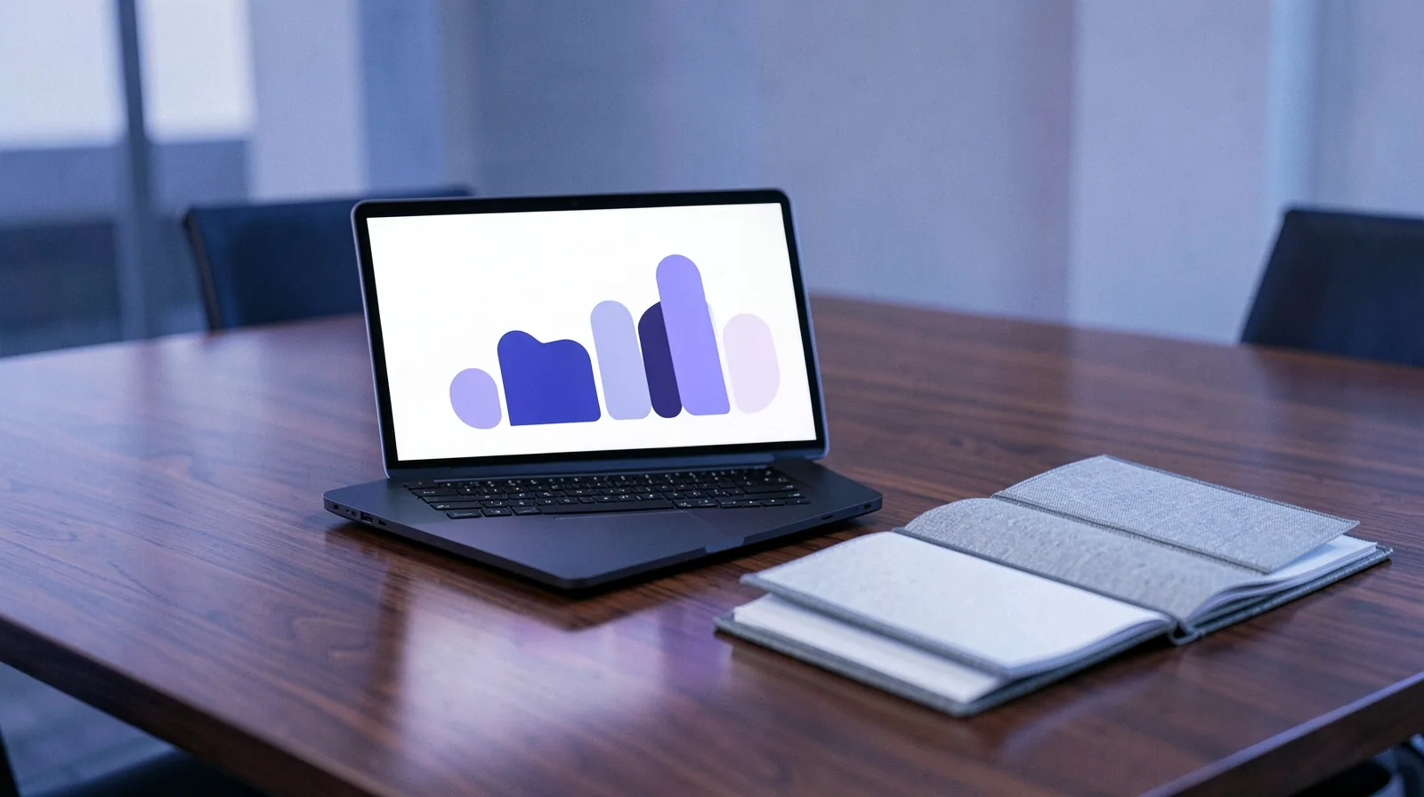 Notebook com um gráfico de barras abstrato na tela ao lado de uma agenda aberta sobre uma mesa de reunião